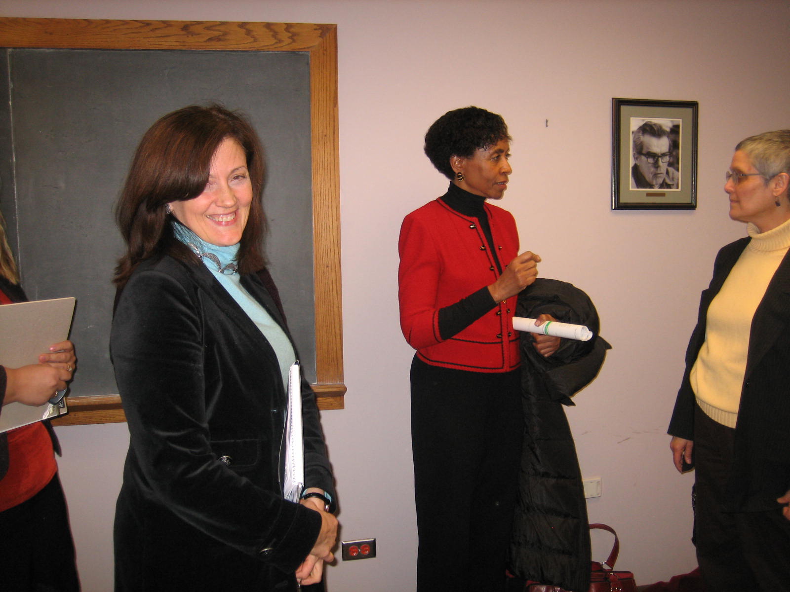 Woman smiling at camera with Bernadette in back ground talking with a woman in a yellow shirt
